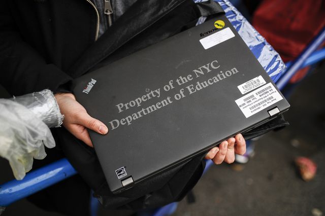 A teen holds a black laptop that says Property of the NYC Department of Education.